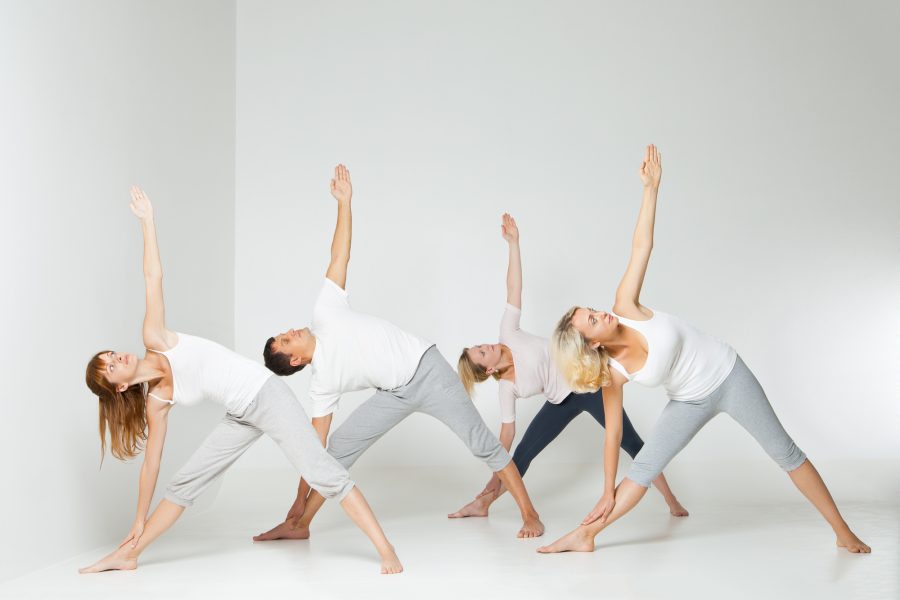 Group of people relaxing and doing yoga in white studio